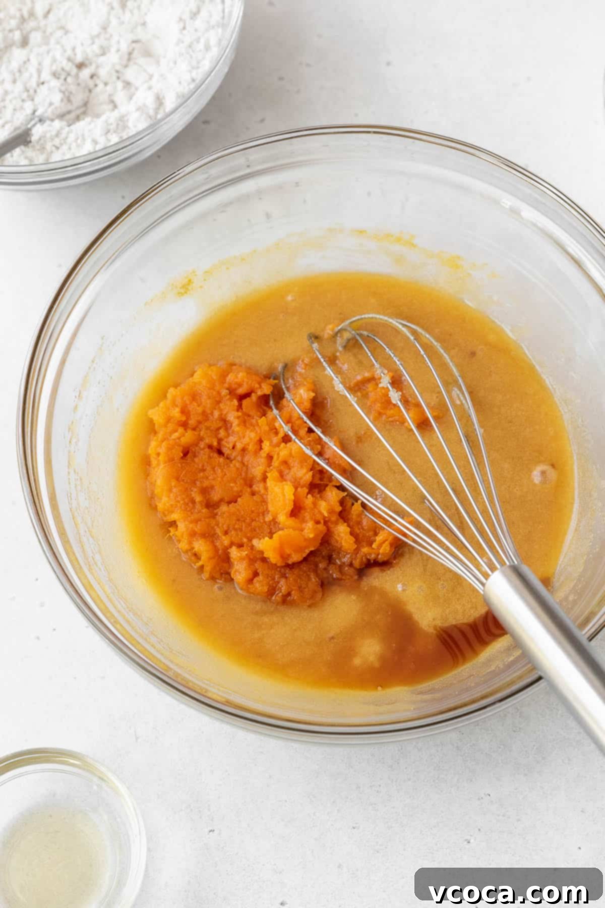 Spiced Sweet Potato Cake with Cashew Frosting 10 Adding mashed sweet potato and vanilla extract to a glass bowl on a white surface.