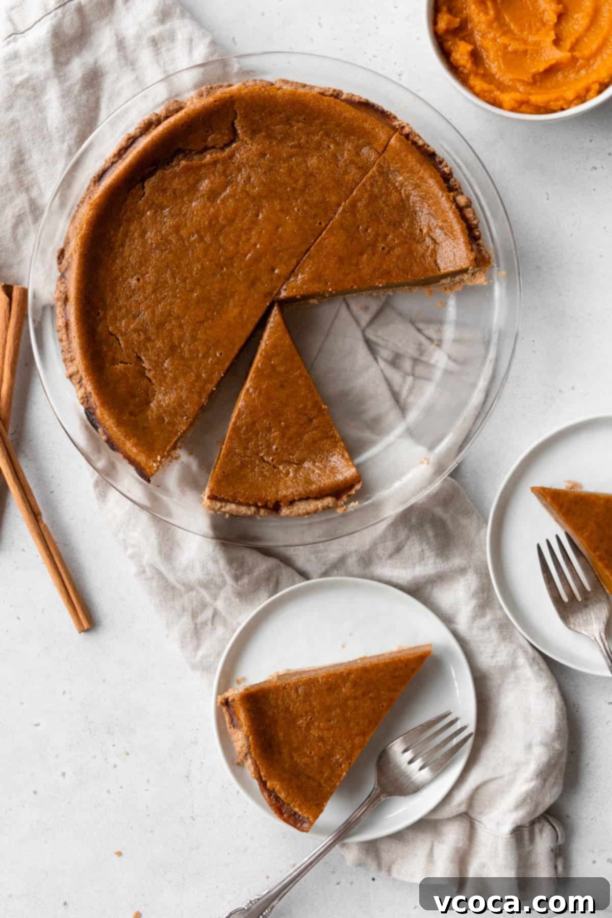 Decadent Vegan Pumpkin Pie 11 A sliced egg-free pumpkin pie on a natural linen with small plates of pie slices placed next to it.