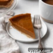 Decadent Vegan Pumpkin Pie 10 Square image of a slice of eggless pumpkin pie on a white dessert plate and a silver fork placed beside it.