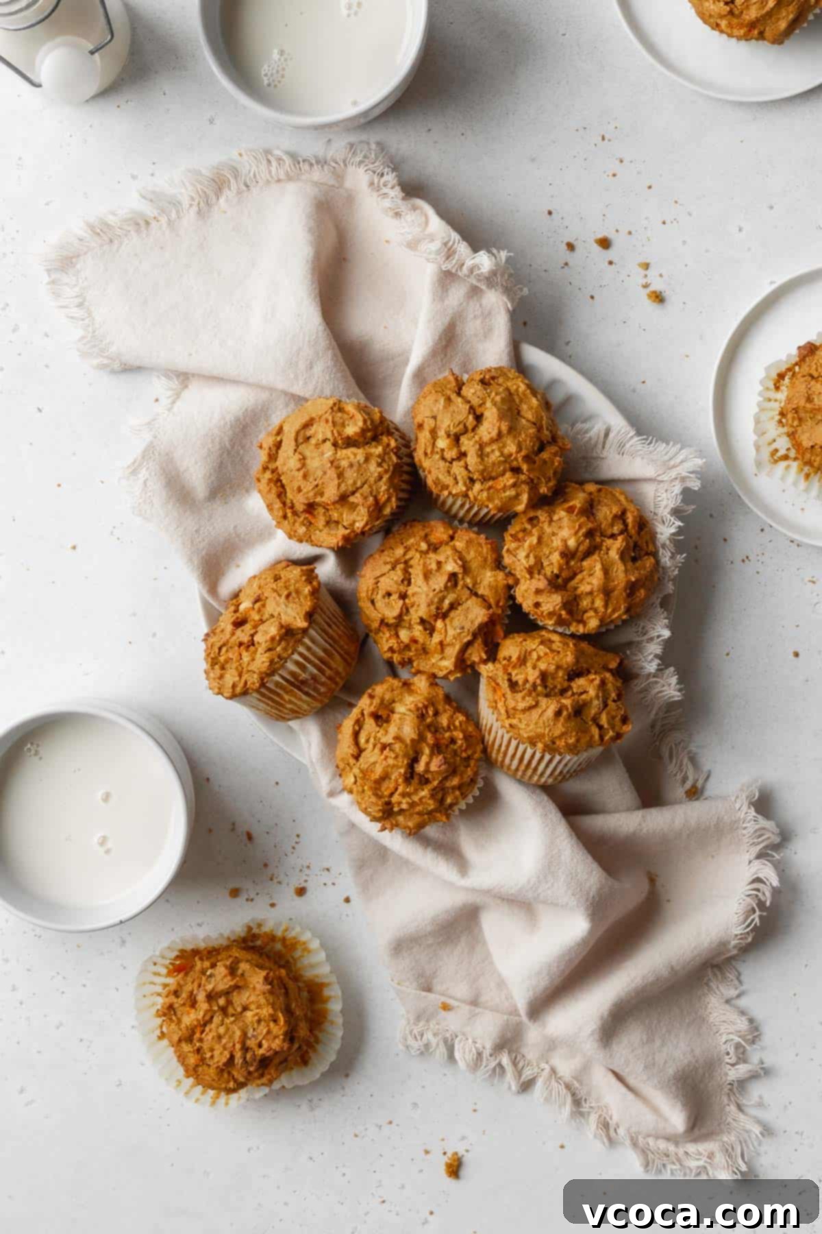 Vibrant Morning Glory Muffins Healthy Gluten Free 4 An overhead hero shot of freshly baked healthy vegan morning glory muffins cooling on a white kitchen towel on a white table, showcasing their golden tops and rustic appeal.