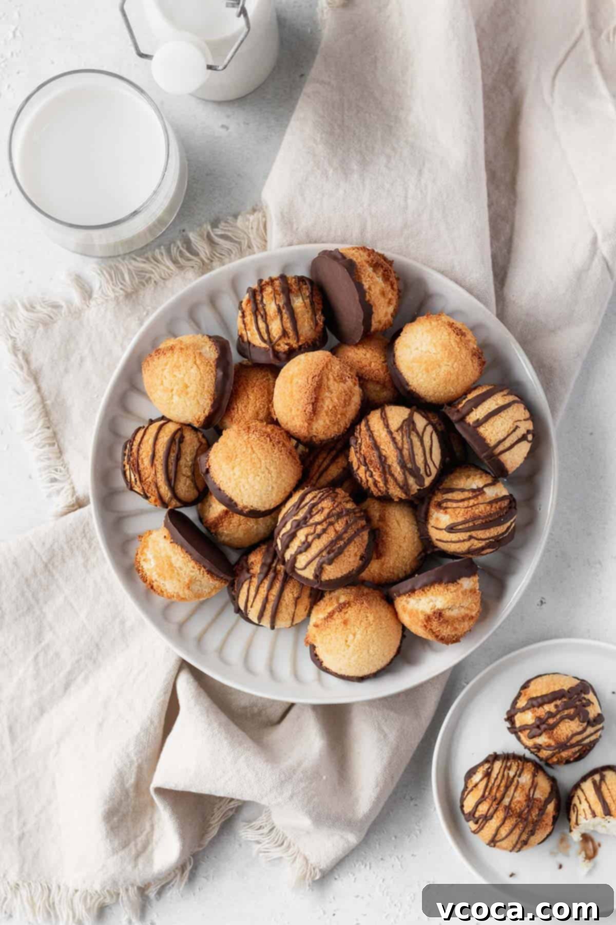 Heavenly Vegan Coconut Macaroons 11 Overhead shot of plain and chocolate drizzled coconut macaroons on a plate with a glass of milk, a smaller plate of macaroons, and a natural linen.