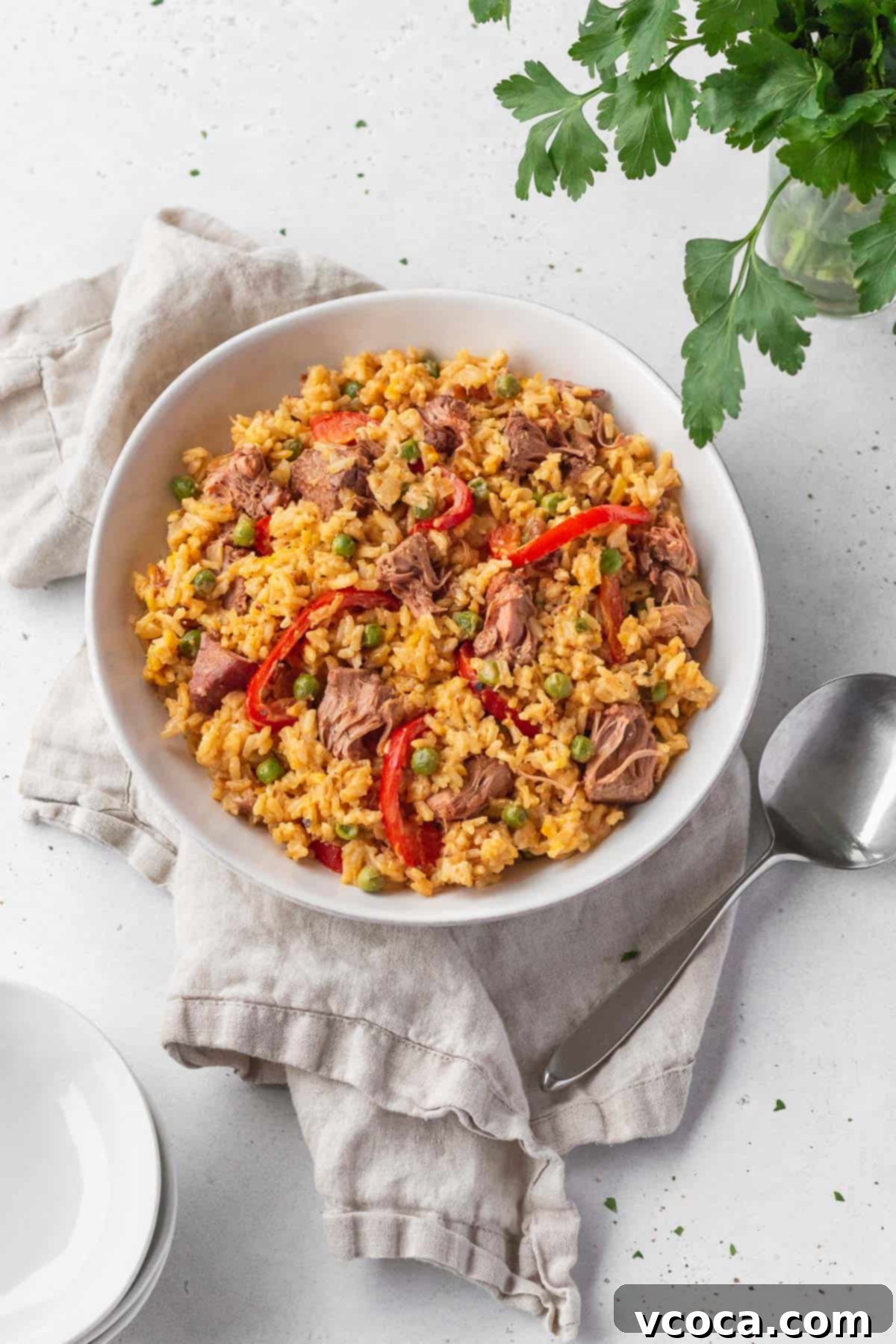 Flavorful Vegan Arroz Valenciana 2 Overhead shot of vibrant vegan Arroz Valenciana in a white bowl with a spoon and natural linen, showcasing its rich colors and texture.