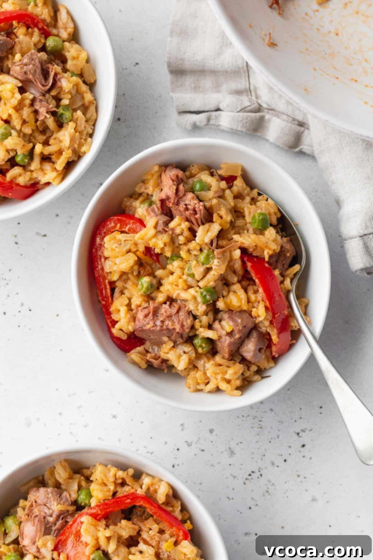 Flavorful Vegan Arroz Valenciana 14 A tantalizing bowl of Valencian style rice with a silver spoon, flanked by two more bowls in the background, creating an inviting tableau.