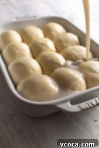 Coconut sauce being poured over risen dough balls in a baking dish