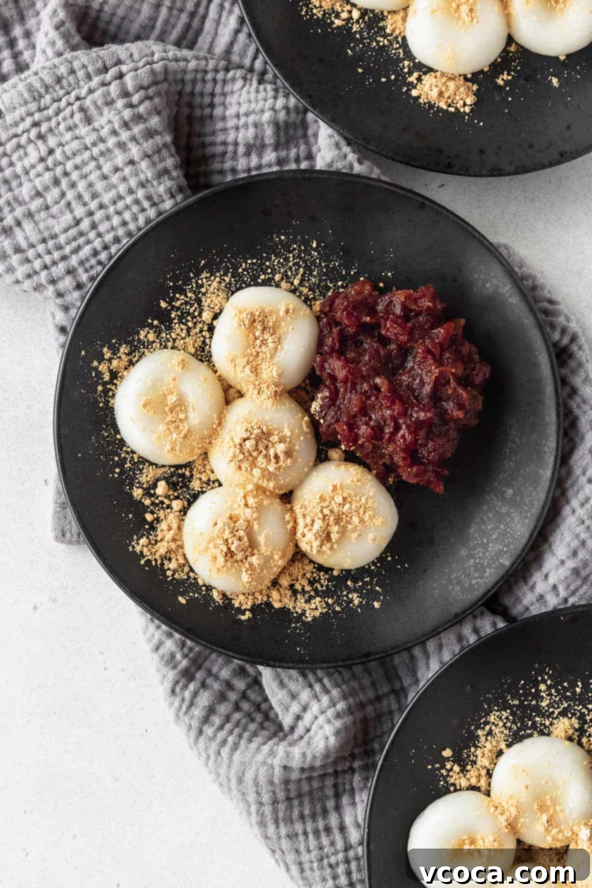 Pearl Rice Dumplings 2 An overhead shot of a black plate with shiratama dango, sweet red bean paste, and kinako sprinkled on top, with two more plates in the corner of the shot.