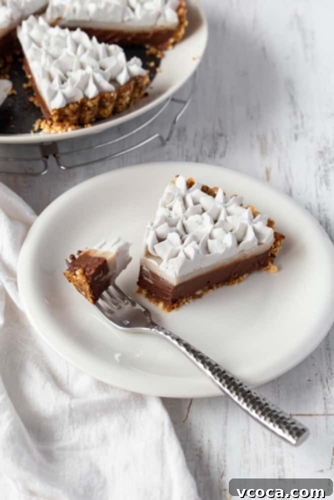 A close-up of a slice of vegan haupia pie on a white plate with a fork poised to take a bite, highlighting the creamy layers and the texture of the crust.