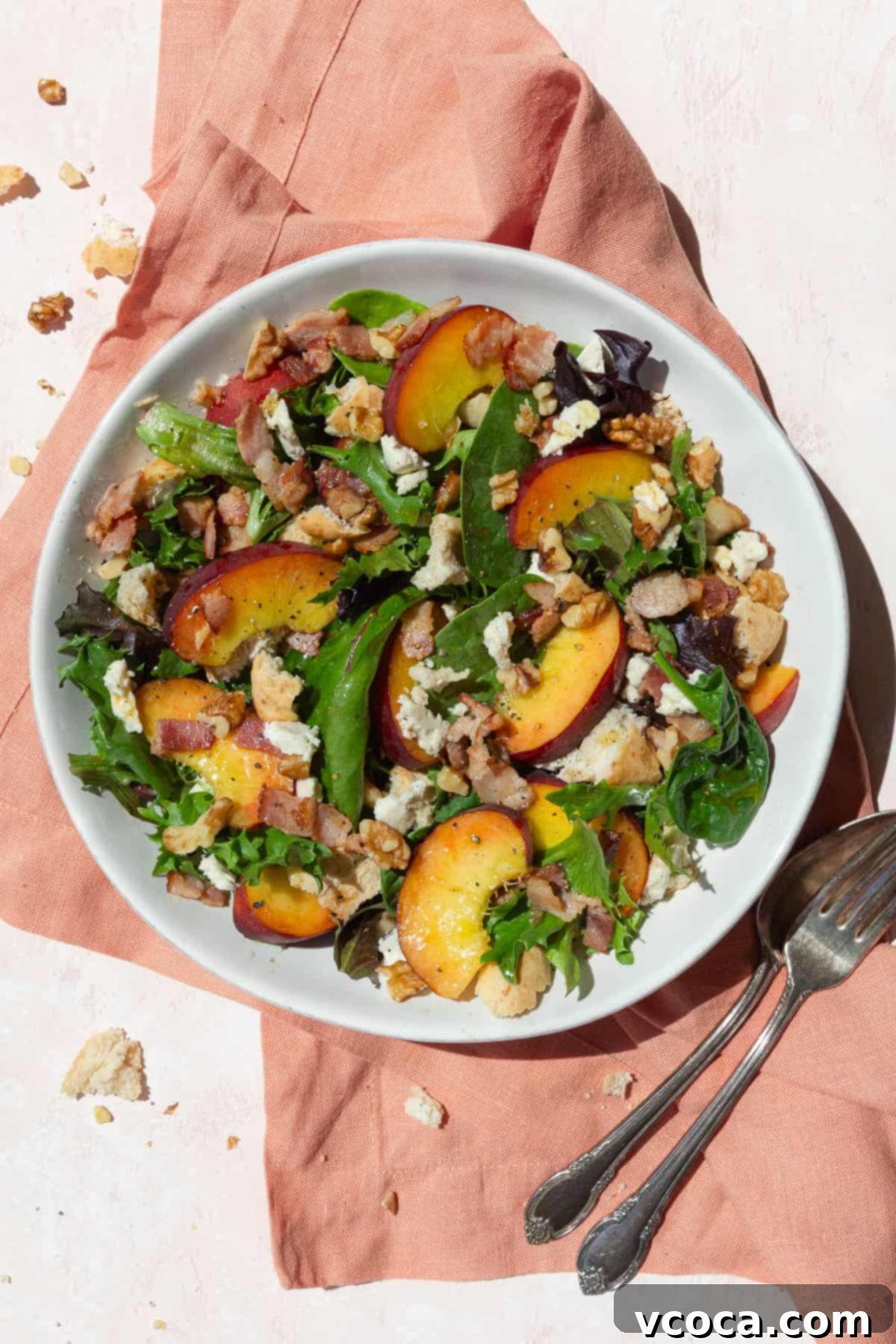 Delicious peach panzanella salad with cheese and crispy bacon in a white bowl, set on a pink linen cloth.