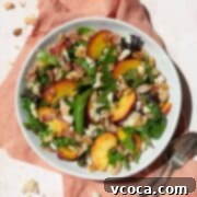 A beautifully arranged peach panzanella salad in a white bowl, resting on a peach-colored linen, with a spoon and fork on the side.