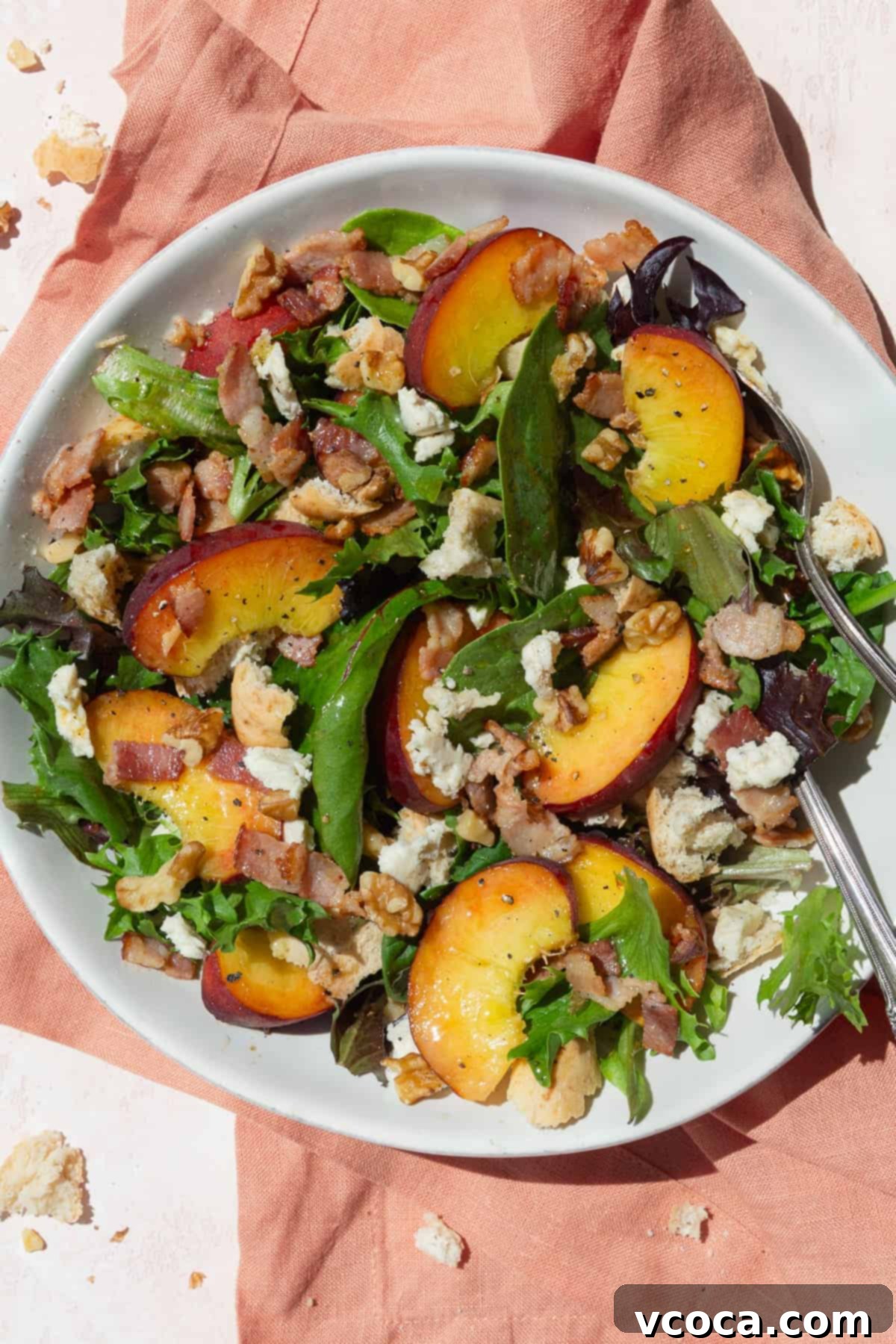 A vibrant peach panzanella salad in a white bowl, presented on a soft peach-colored background, highlighting its fresh ingredients.
