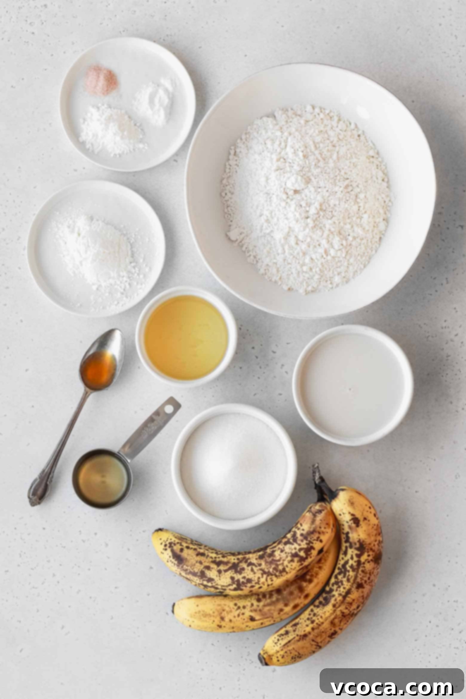 Ingredients for homemade banana cupcakes, including flour, sugar, mashed bananas, oil, milk, and vanilla, neatly arranged in bowls.