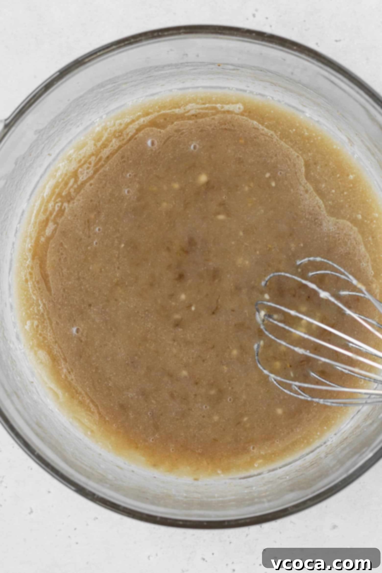 A bowl containing a mixture of wet ingredients for banana cupcakes: oil, mashed banana, sugar, milk, apple cider vinegar, and vanilla extract.