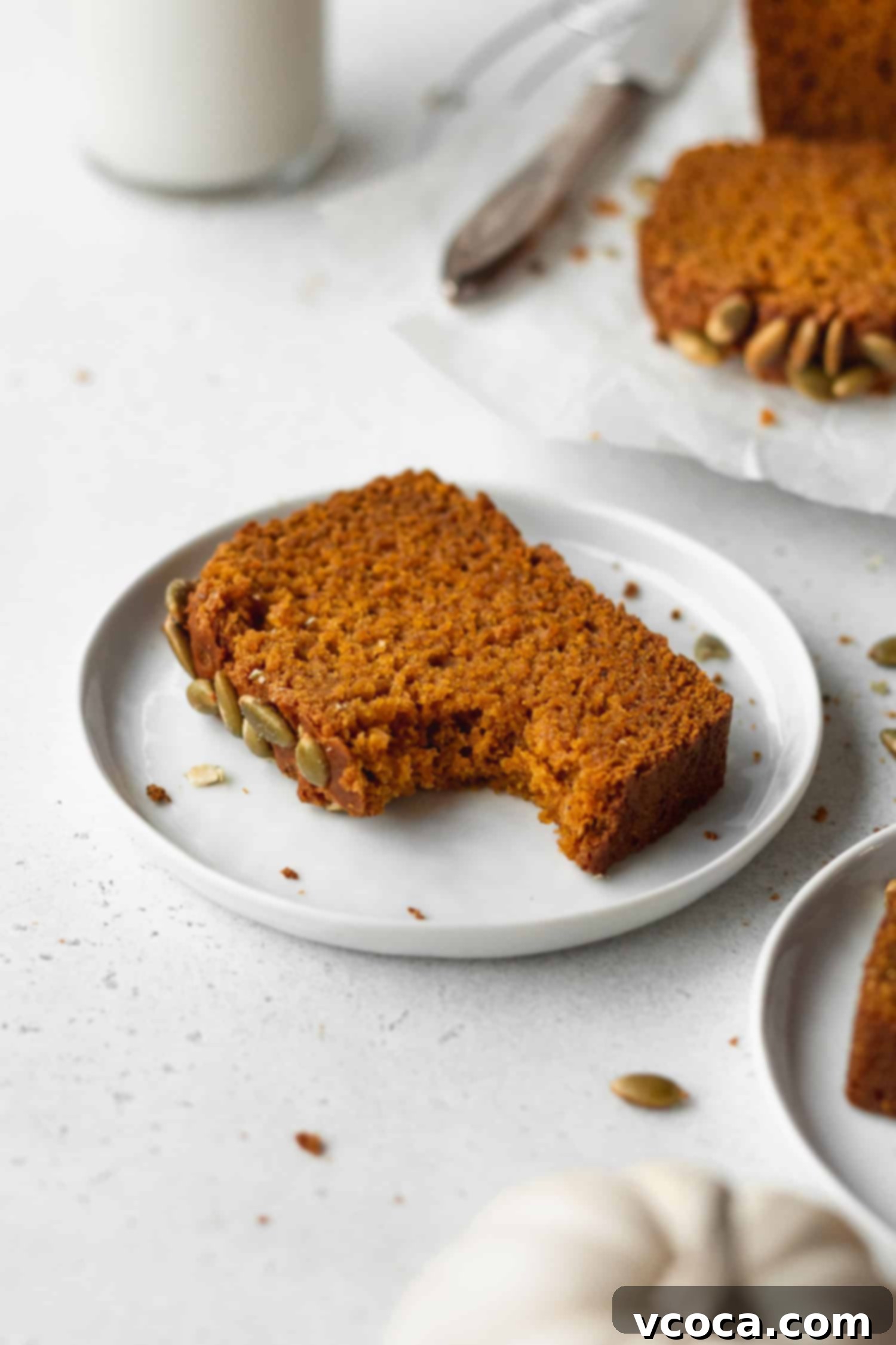 A close-up shot of a bitten slice of super moist gluten-free pumpkin bread on a plate, highlighting its tender crumb and spiced flavor.