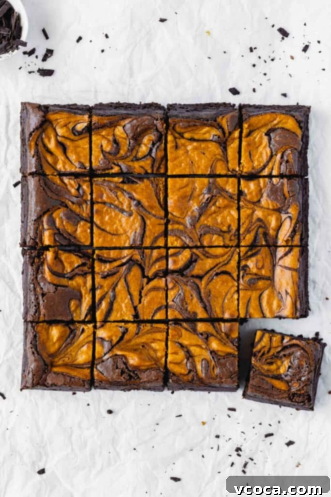 Swirled Pumpkin Cheesecake Brownies 2 Pumpkin cheesecake brownies cut into squares on parchment paper, showcasing the beautiful swirl.