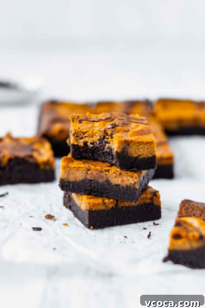 Swirled Pumpkin Cheesecake Brownies 6 A stack of three pumpkin cheesecake brownies with more brownies scattered around, highlighting their inviting appeal.