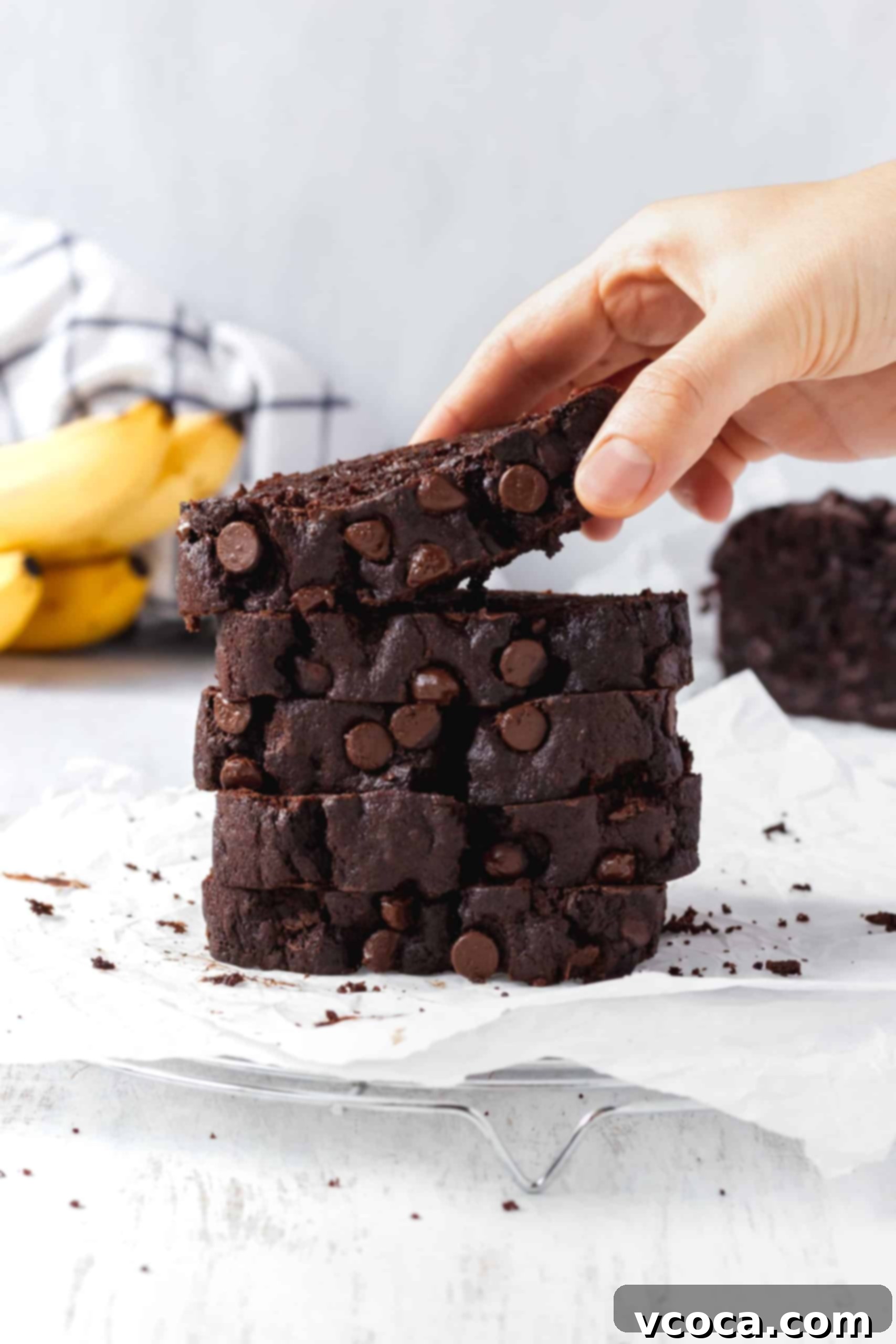 Decadent Chocolate Banana Loaf 2 A stack of incredibly moist and rich double chocolate banana bread slices, with a hand reaching for a piece, showcasing the luscious chocolate chips and tender crumb. Perfect for an indulgent breakfast or snack.