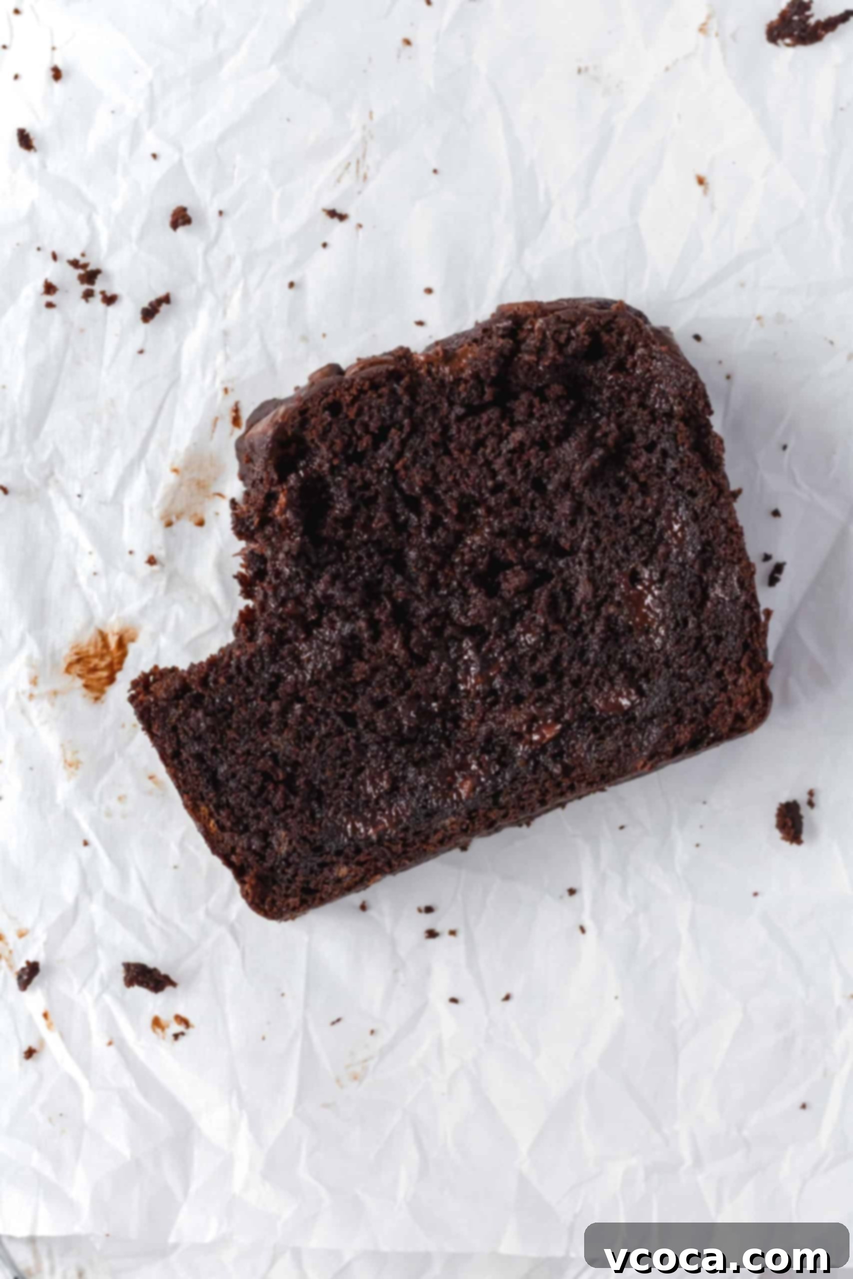 Decadent Chocolate Banana Loaf 3 A perfectly baked slice of double chocolate banana bread on parchment paper, showing its deep brown color, incredibly moist interior, and visible melted chocolate chips. A bite has been taken out, revealing the soft, tender texture.