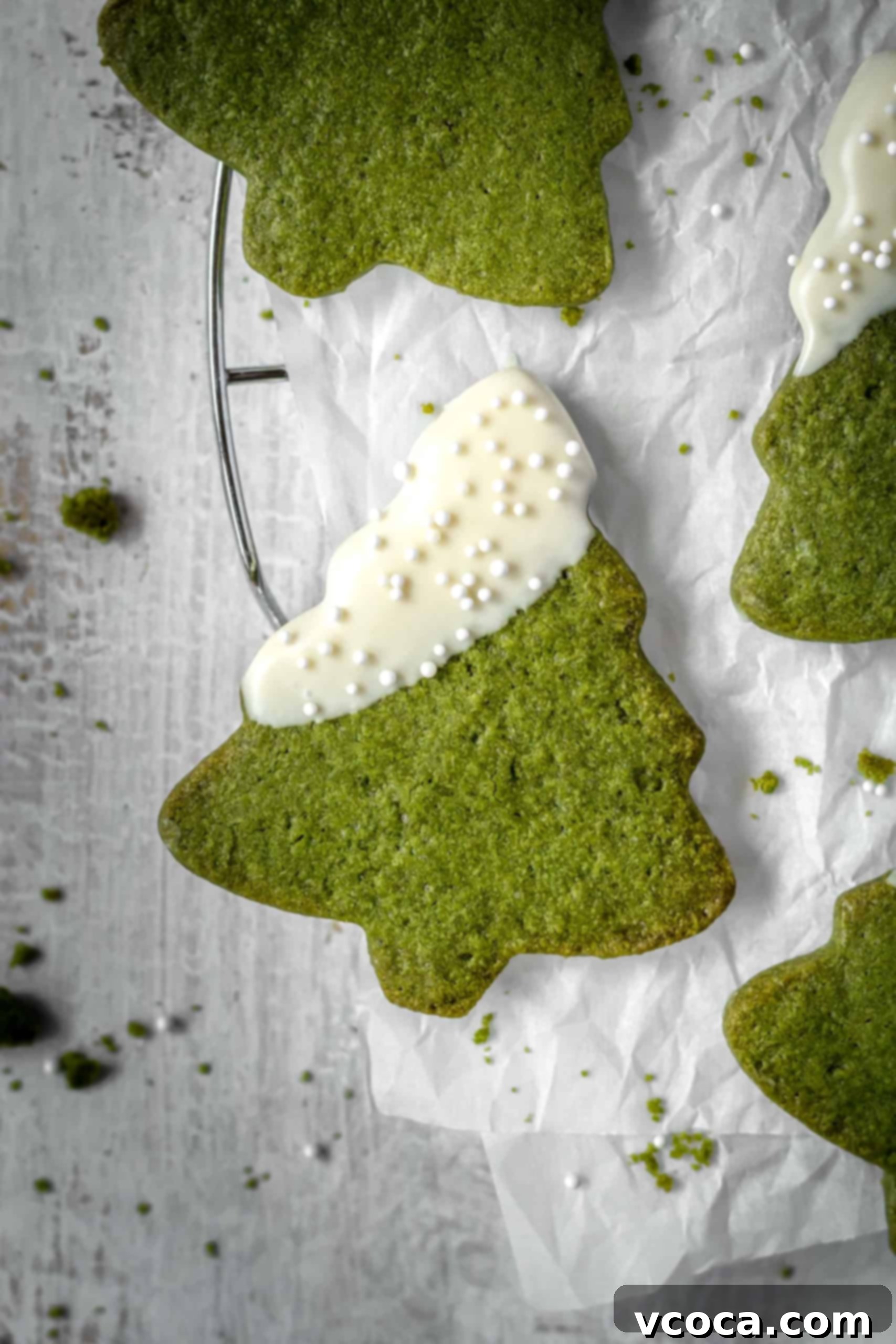 Festive Matcha Christmas Tree Cookies 3 Close-up of freshly decorated Matcha Christmas Tree Cookies with melted white chocolate and festive sprinkles, showcasing their perfect shape and natural green color for easy holiday baking.