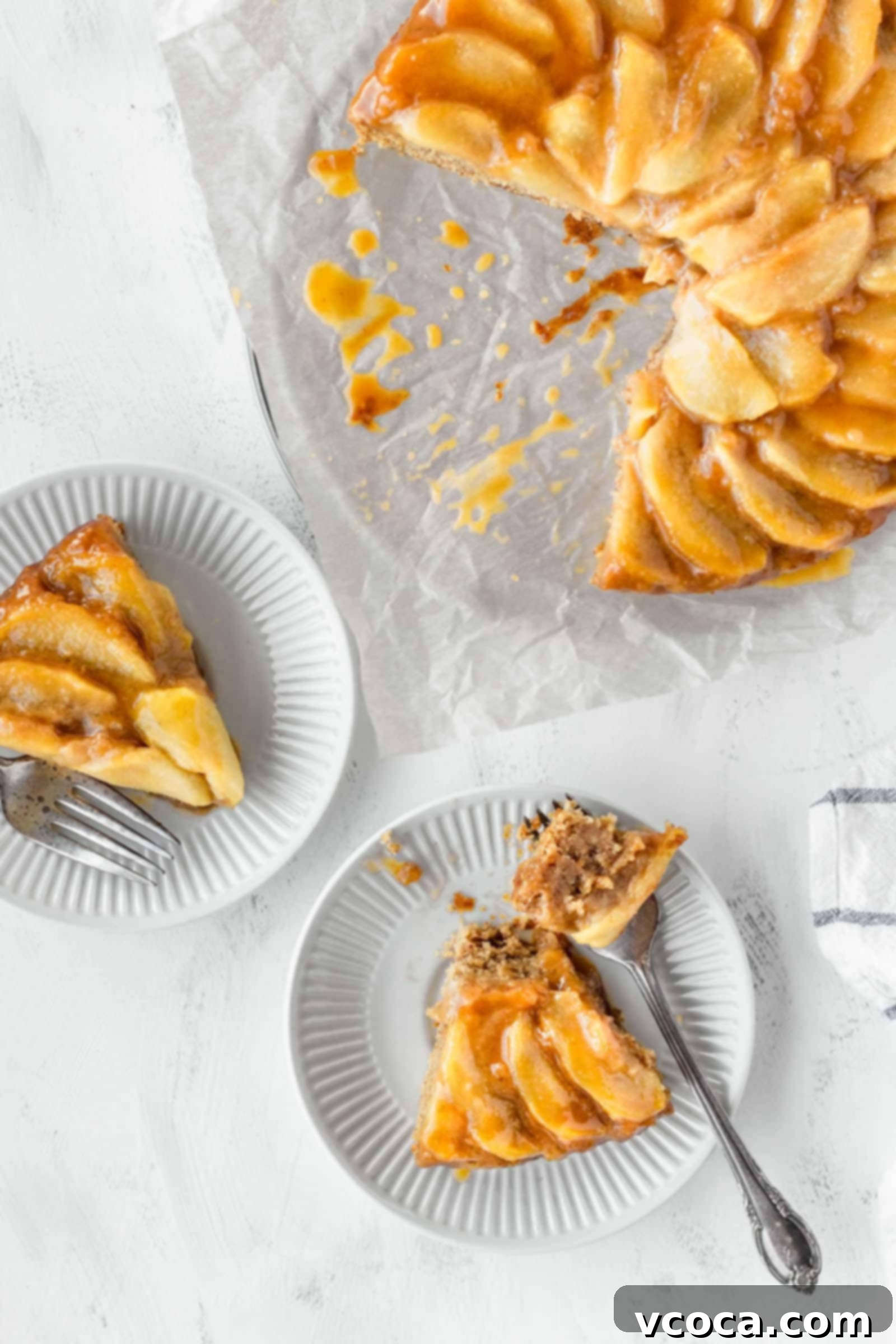 Pure Plant Apple Cake Bliss 4 Two slices of vegan apple cake on small white plates next to the whole cake, highlighting its golden crust and juicy apples.