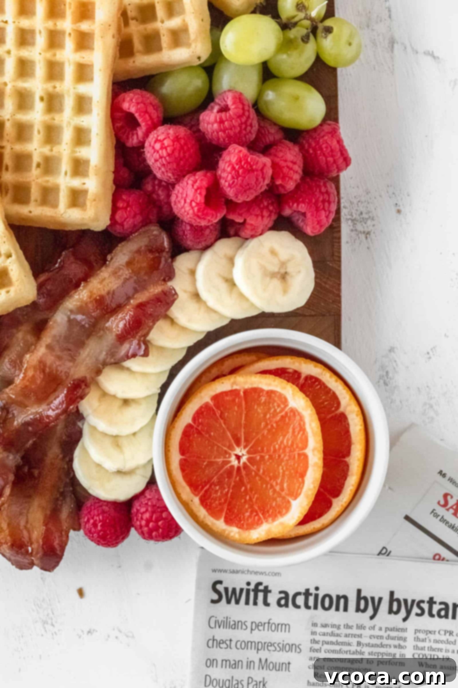 Your Perfect Gluten-Free Waffle Board for Two 3 Close-up of green grapes, red raspberries, sliced bananas, oranges, and bacon on a breakfast charcuterie board