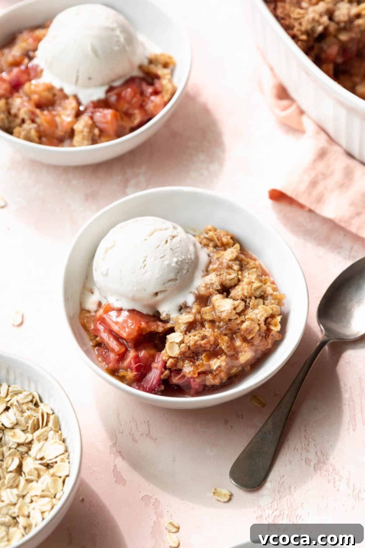 Sweet & Tart Gluten-Free Rhubarb Crisp 2 Two bowls of vegan, gluten-free rhubarb crisp with vanilla ice cream next to the larger casserole dish filled with the rest of the dessert.