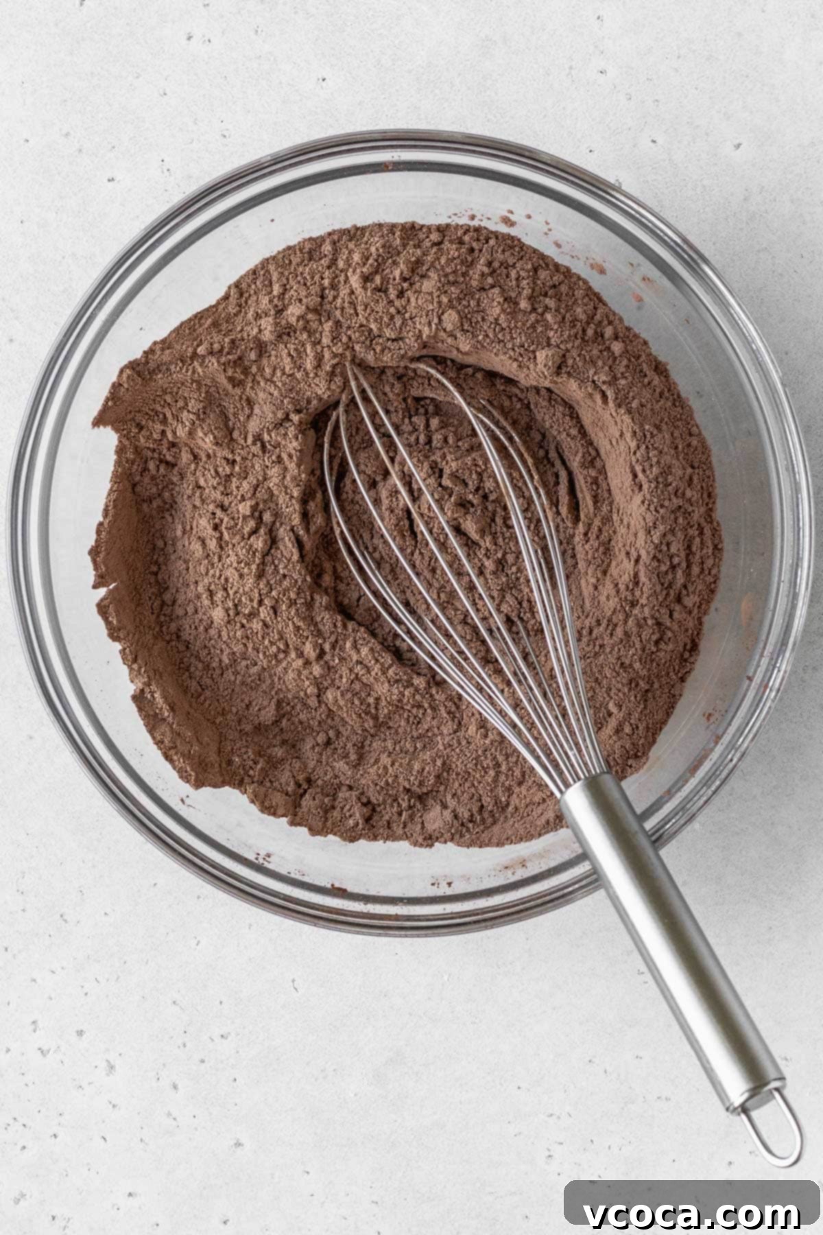 Decadent Gluten-Free German Chocolate Dream 6 Dry ingredients for a gluten-free chocolate cake in a glass bowl with a silver whisk.