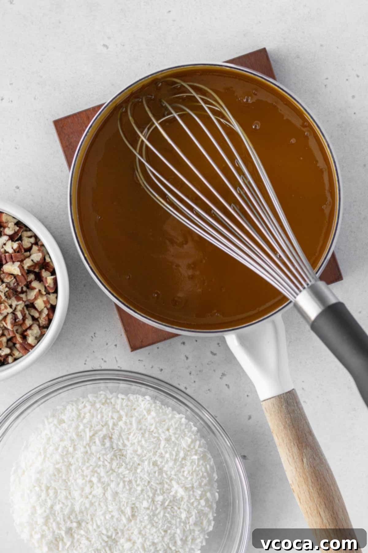 Decadent Gluten-Free German Chocolate Dream 10 German chocolate frosting mixture being cooked in a saucepan with a bowl of shredded coconut and a bowl of chopped pecans next to it.