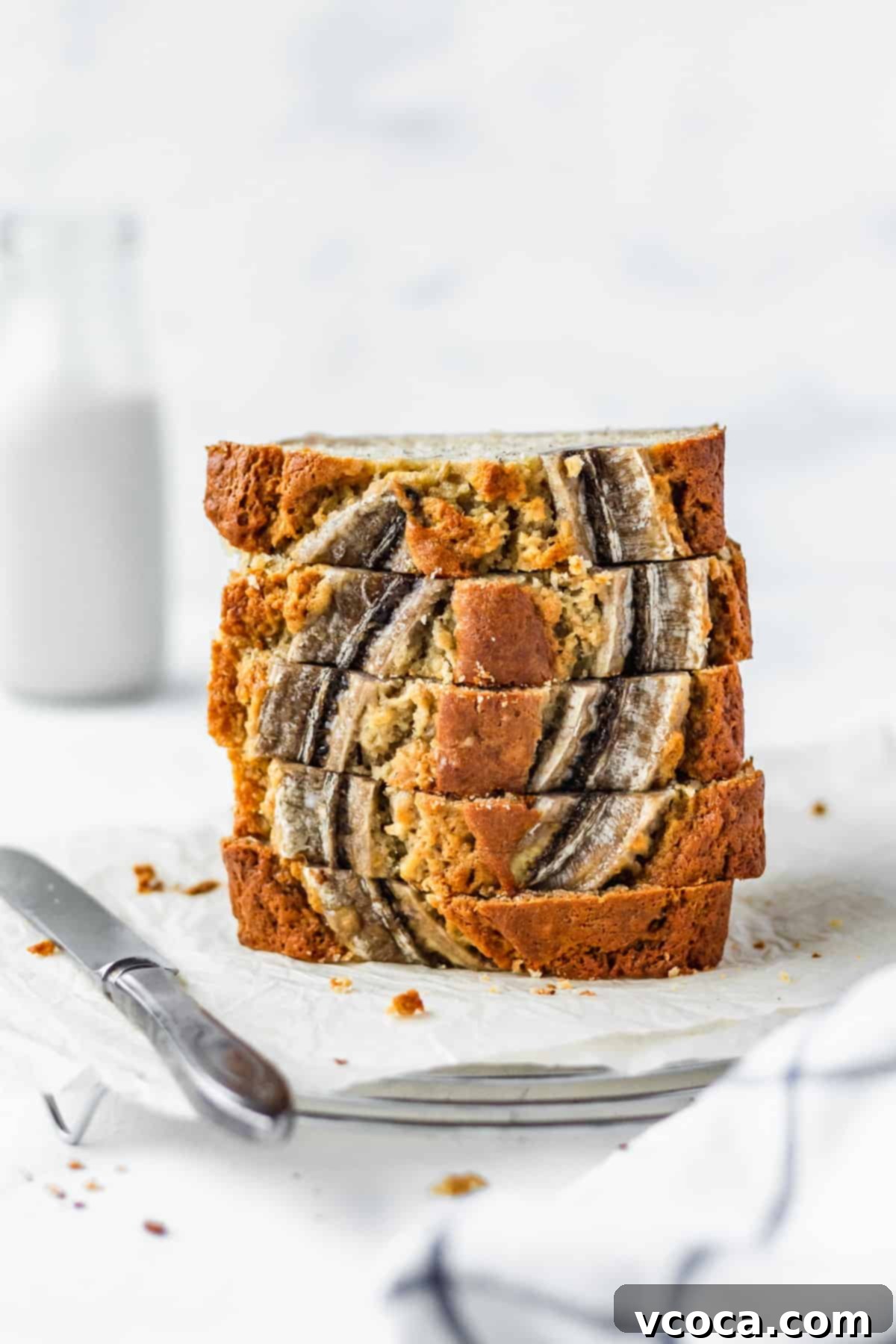 A stack of moist banana bread on parchment paper with a bottle of milk in the background.