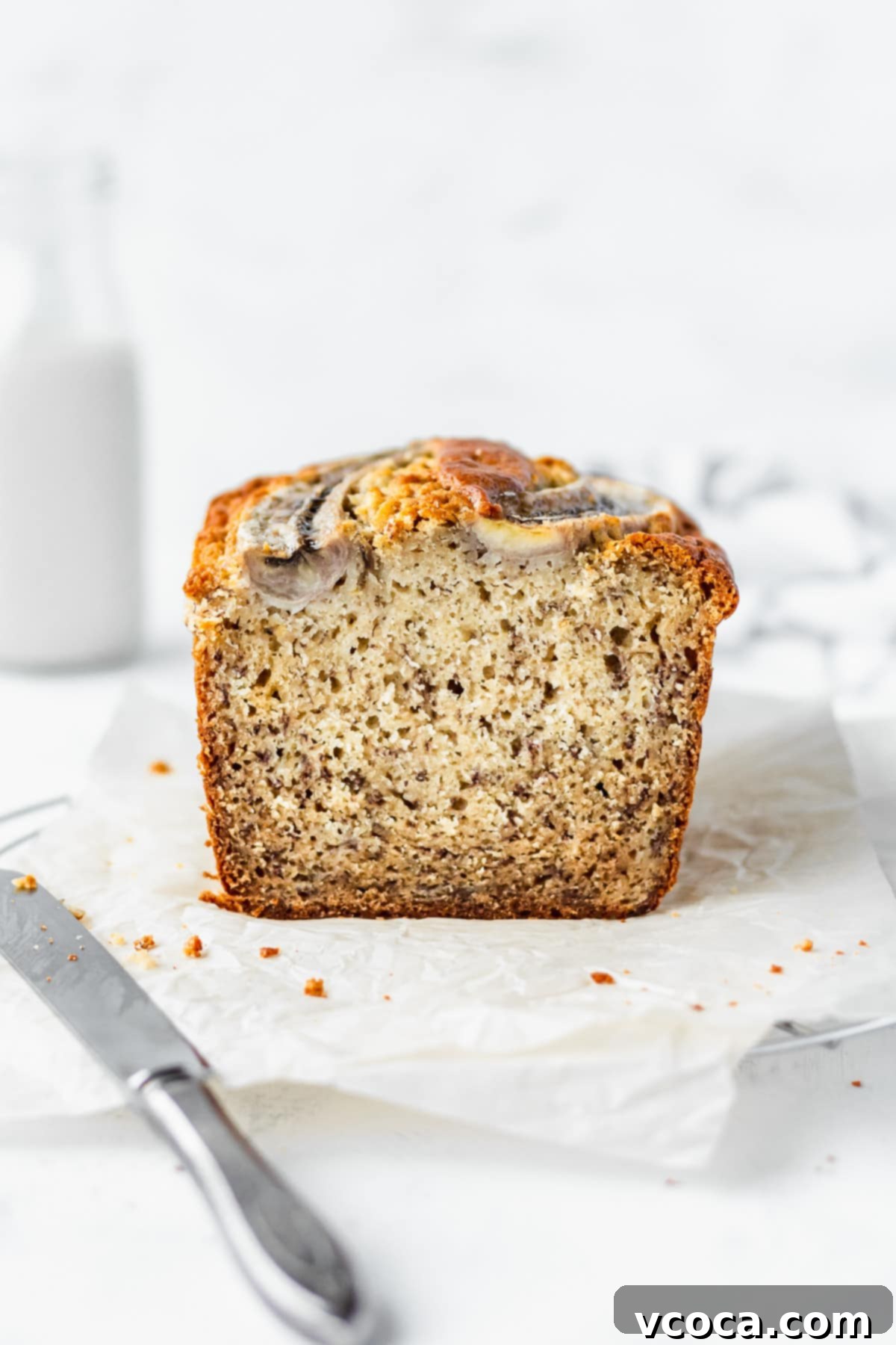 A sliced loaf of moist banana bread with a knife next to it.