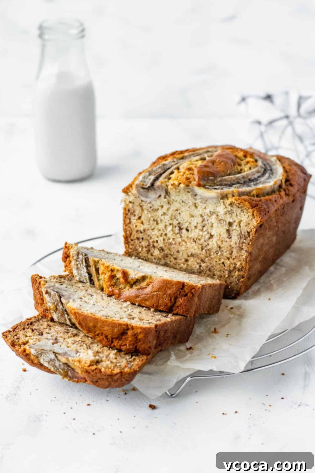 A loaf of homemade banana bread on parchment paper with three slices laid in front.