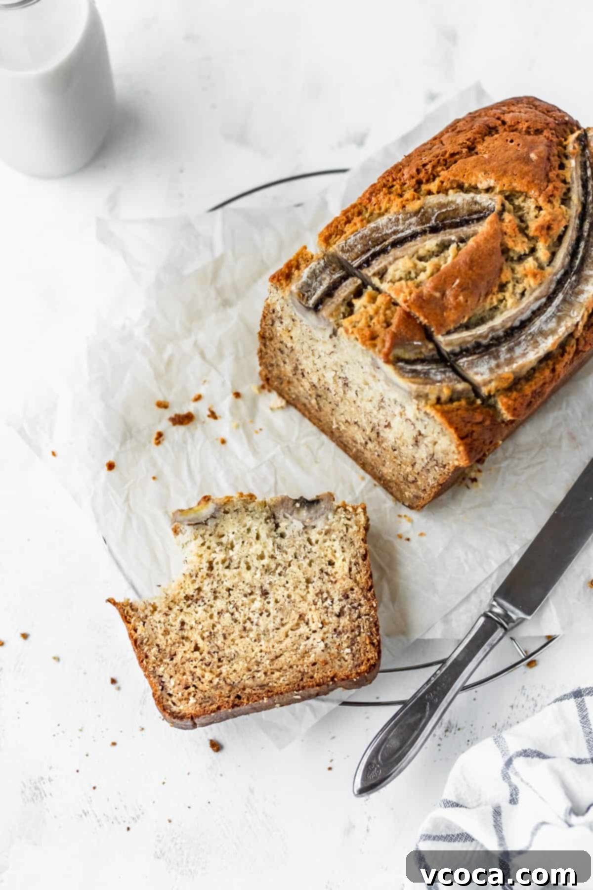 A loaf of banana bread with a bitten slice laying in front.