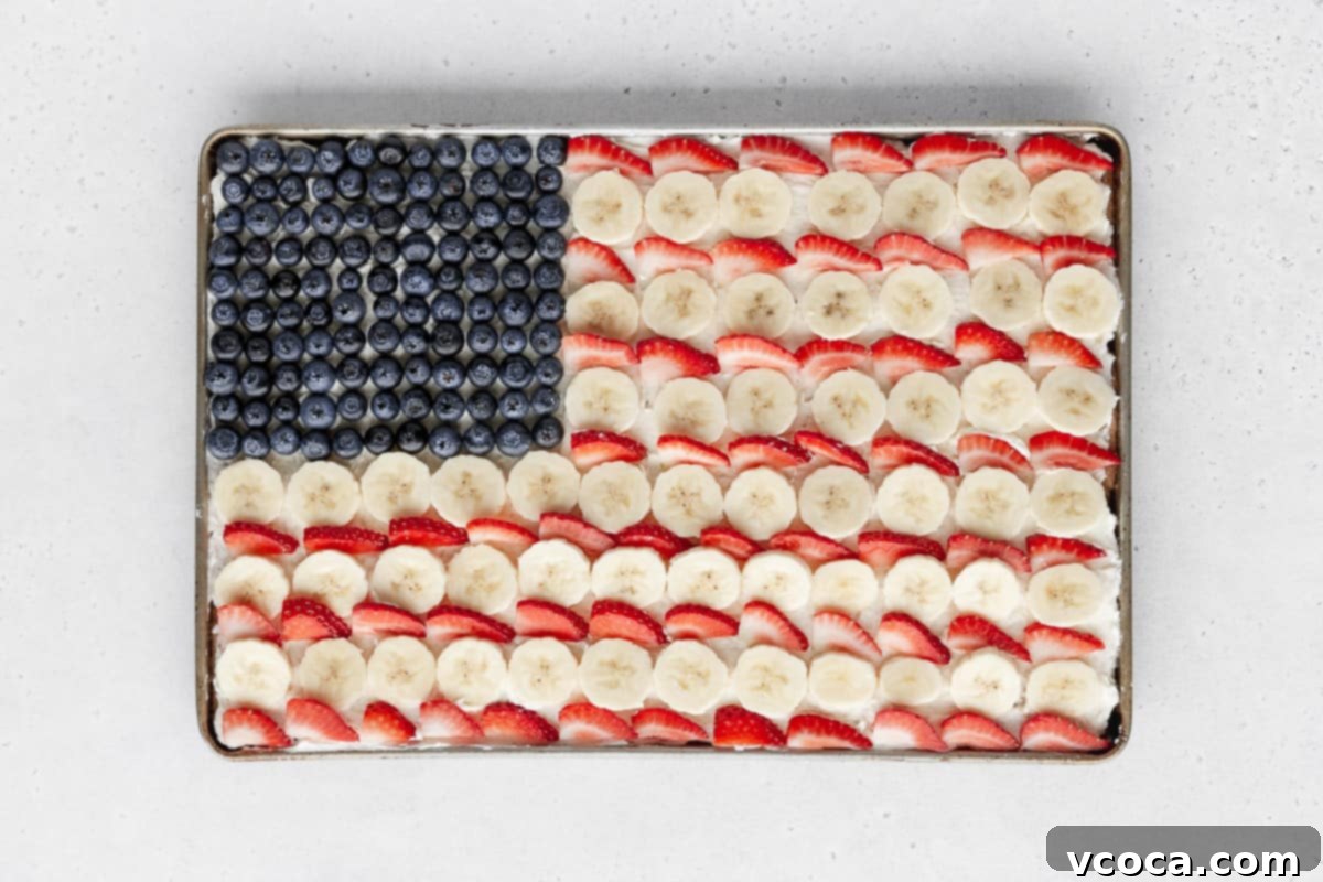 Festive 4th of July Fruit Pizza 12 Alternating rows of sliced bananas and strawberries added to fill out the rest of the sheet pan, completing the American flag fruit cookie pizza design.