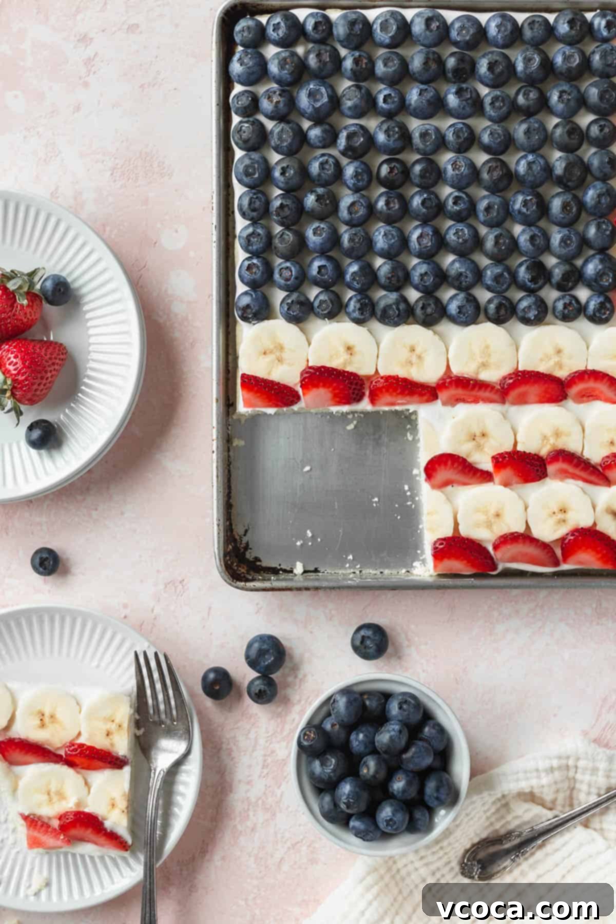 Festive 4th of July Fruit Pizza 13 A sheet pan of patriotic American flag cookie cake with one slice neatly taken out, showcasing the layers of cookie, frosting, and fruit.