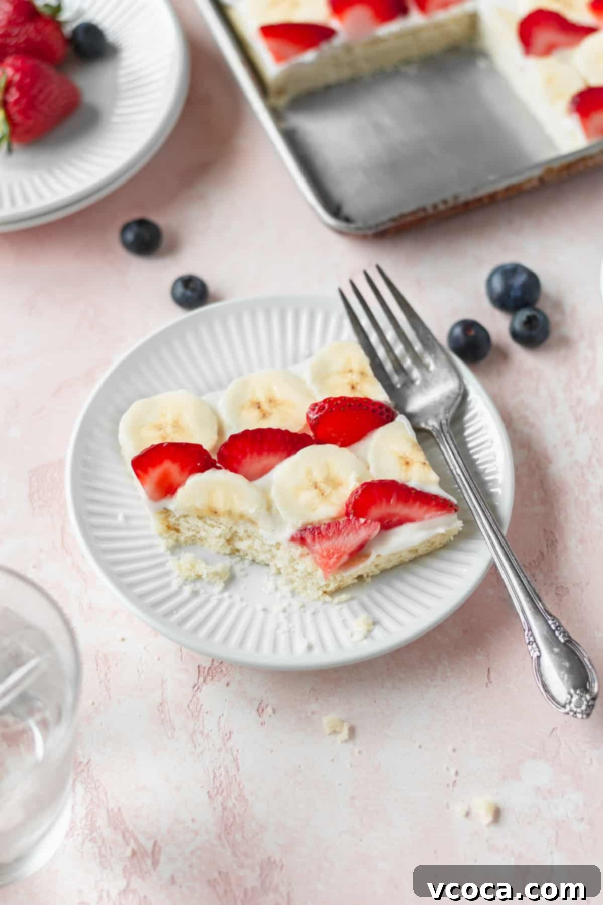 Festive 4th of July Fruit Pizza 14 A perfectly cut slice of American flag fruit pizza displayed on a white dessert plate, accompanied by a silver fork.
