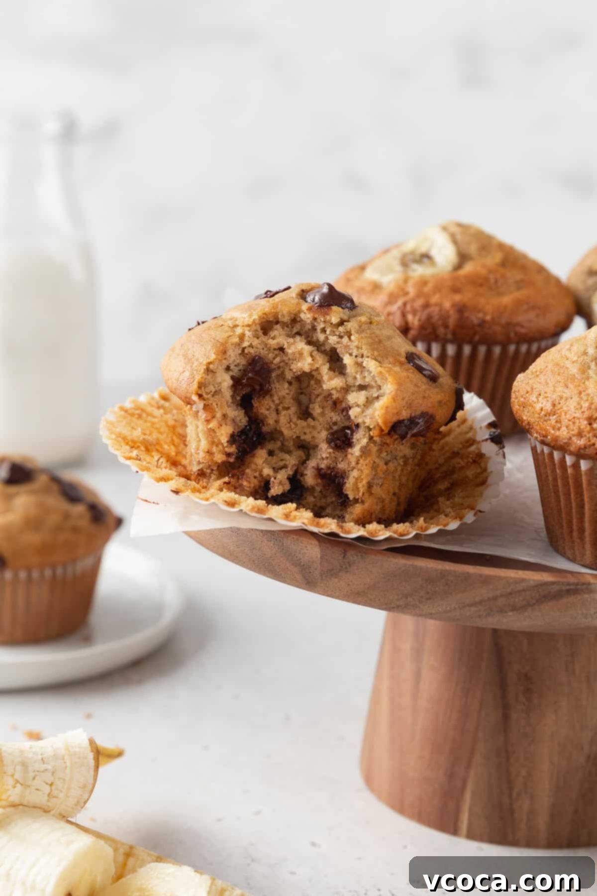 Irresistible Gluten-Free Banana Muffins 4 A bitten gluten free banana chocolate chip muffin on a wooden cake stand.