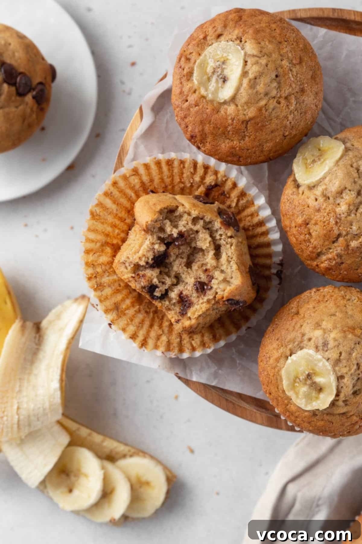 Irresistible Gluten-Free Banana Muffins 5 A bitten chocolate chip banana muffin on a paper liner surround by three more muffins.