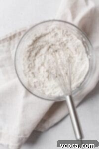A glass bowl of dry ingredients with a whisk.