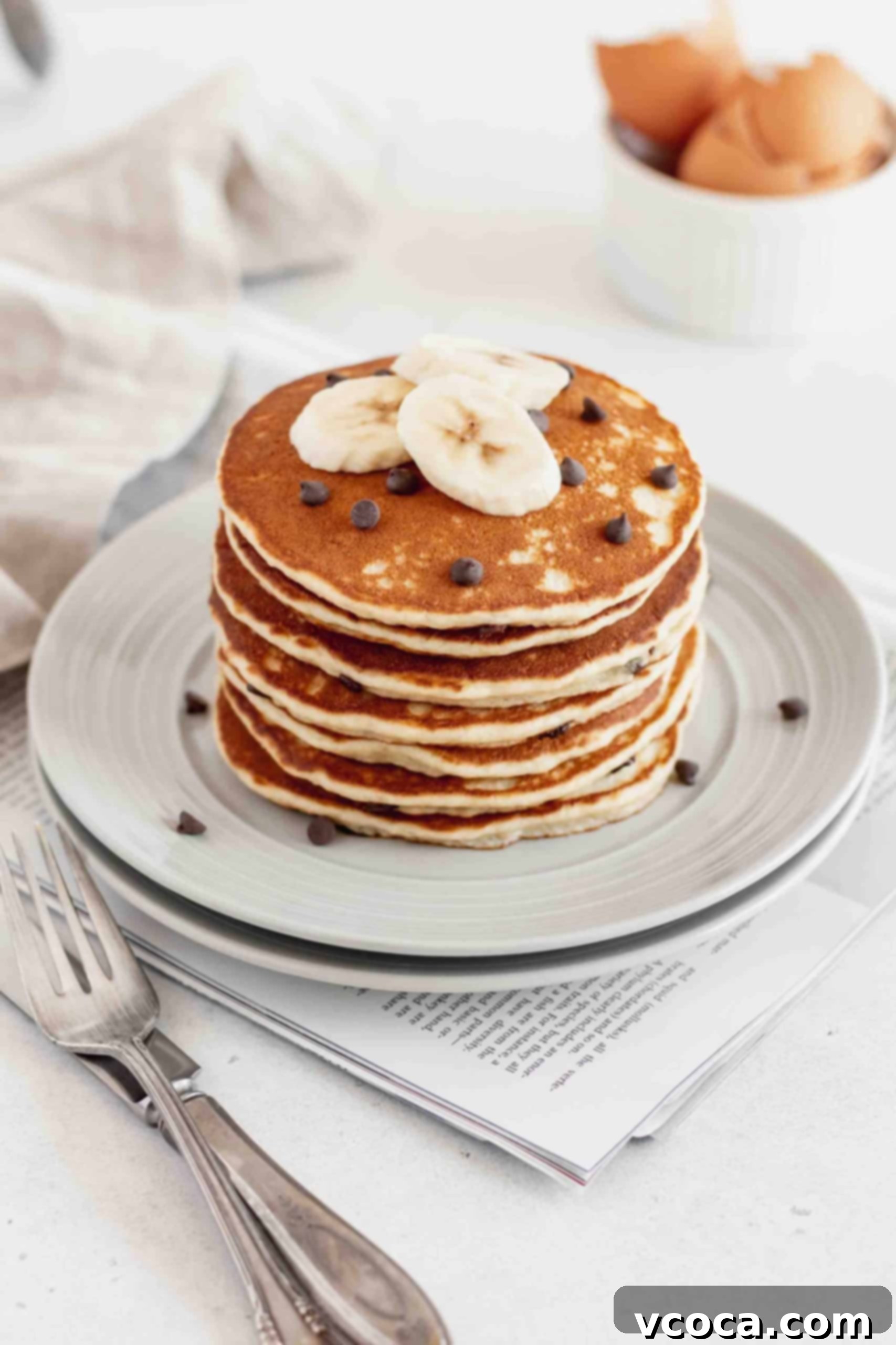 Fluffy Gluten-Free Banana Pancakes 5 A beautifully composed shot of two gray plates, each holding a generous stack of golden-brown gluten-free banana chocolate chip pancakes. The warm, inviting presentation suggests a cozy and satisfying breakfast or brunch.