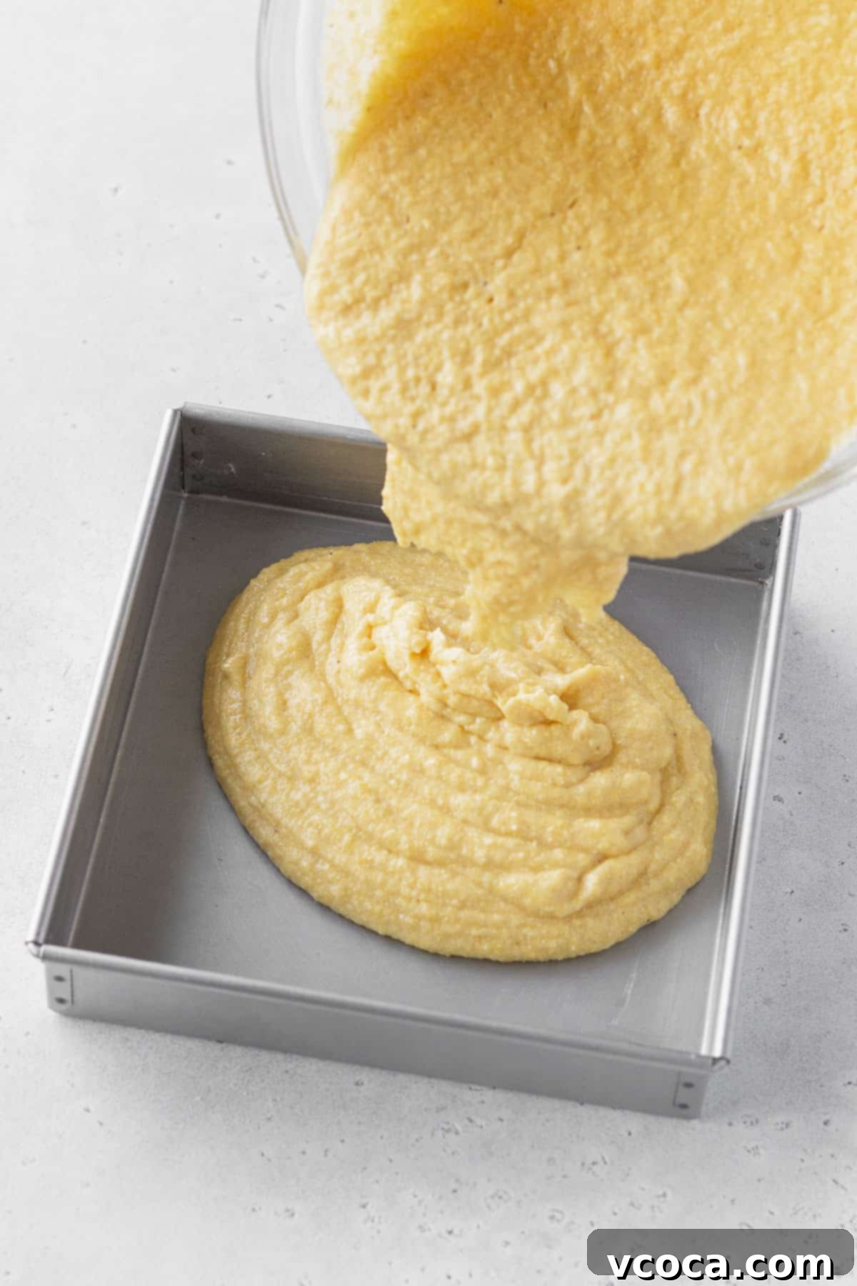 Golden Gluten Free Cornbread 10 Pouring gluten-free cornbread batter into a prepared 8x8-inch baking tin for baking, ensuring even distribution.