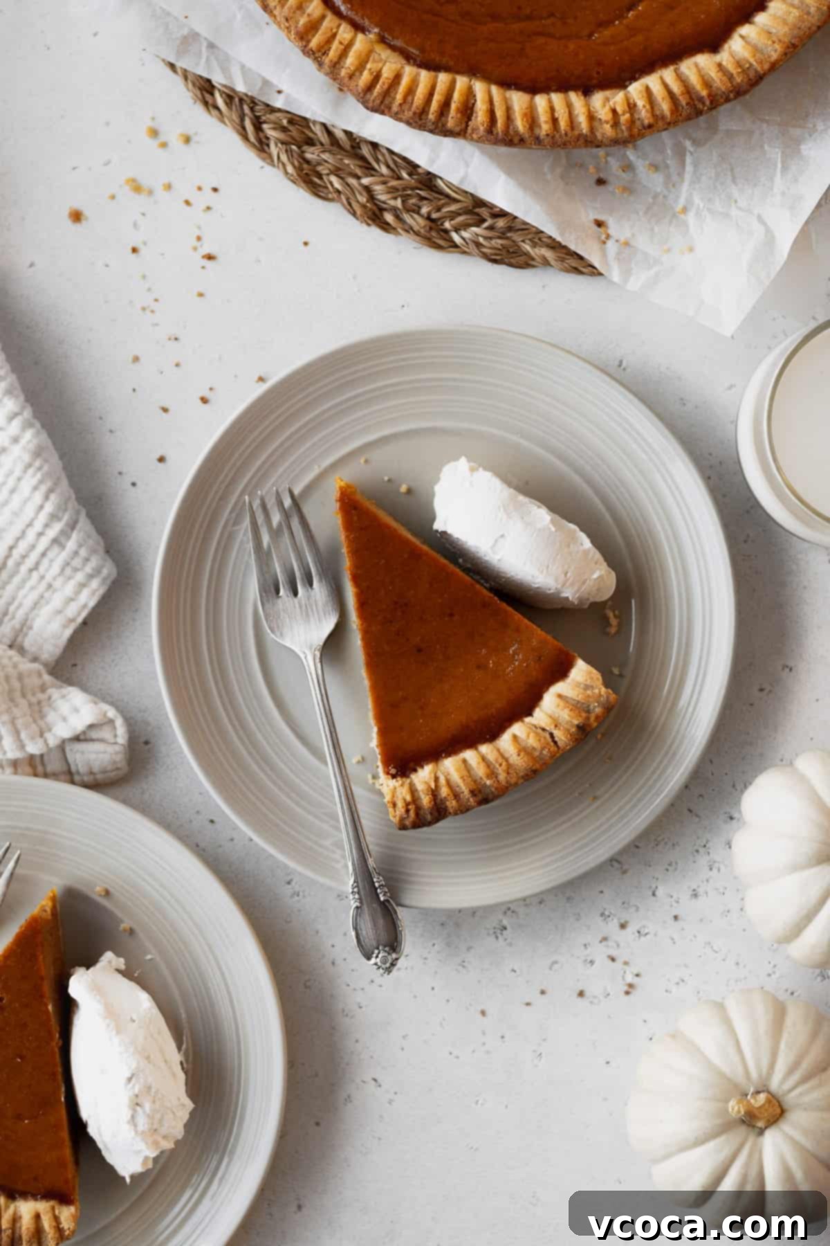 Wholesome Vegan Pumpkin Perfection 18 Overhead shot of a slice of dairy-free pumpkin pie with whipped cream and a fork on a plate surrounded by plates and white pumpkins.