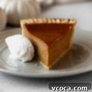 Wholesome Vegan Pumpkin Perfection 20 A slice of dairy-free pumpkin pie on a grey plate with a whipped coconut cream on the side.