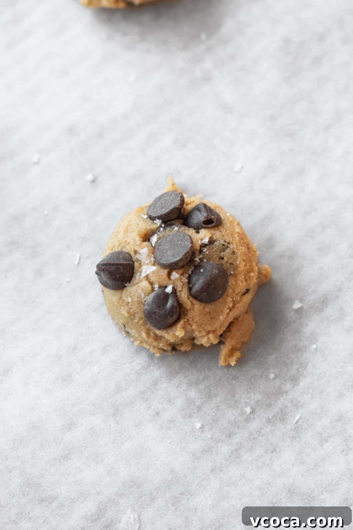 Irresistible Gluten-Free Chocolate Chip Cookies 9 closeup of a ball of cookie dough that has been topped with extra chocolate chips and a sprinkle of coarse salt.