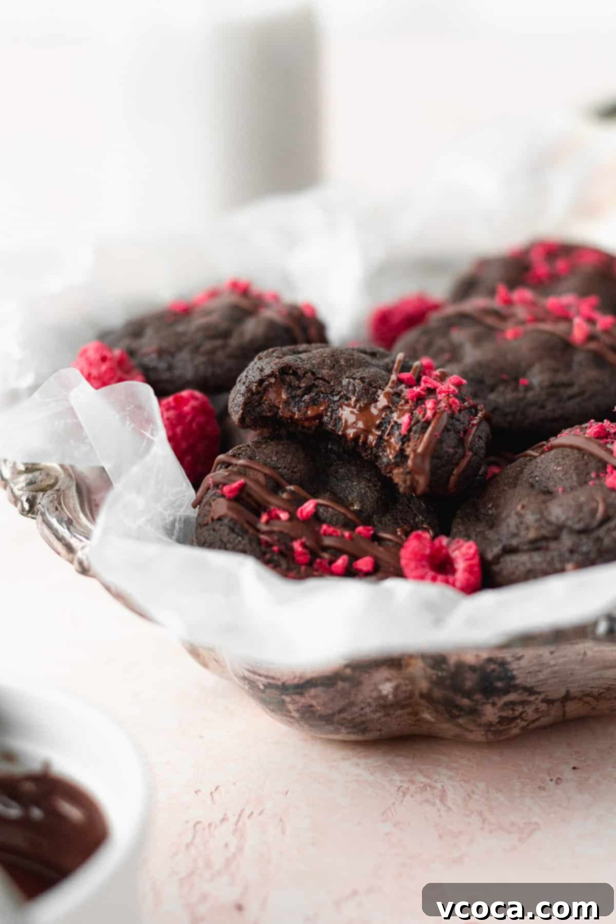 A silver dish with gluten free chocolate cookies, with a bitten cookie on top showing melted chocolate chips and its fudgy interior.
