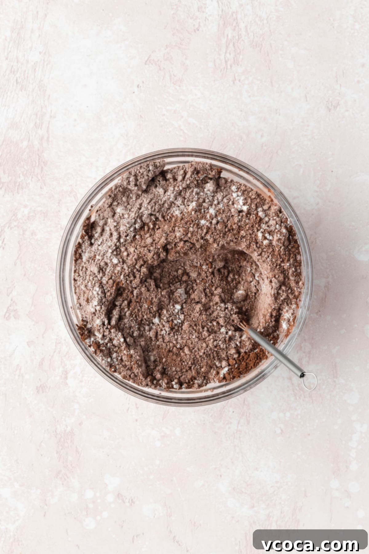 Flour, cocoa powder, salt, baking soda, and baking powder mixed together in a glass bowl. The dry ingredients are light brown and well combined.