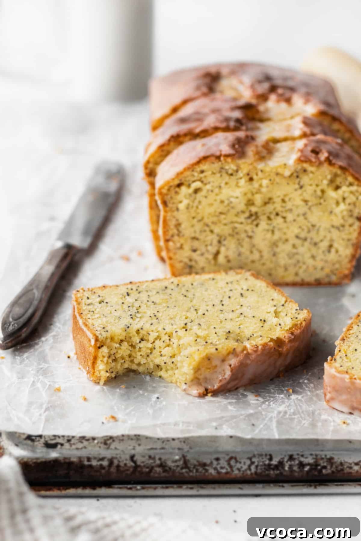 Zesty Gluten-Free Lemon Poppy Seed Cake 6 A bitten slice of gluten free lemon bread with the loaf in the background.