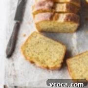 Zesty Gluten-Free Lemon Poppy Seed Cake 7 A slice of gluten free lemon poppy seed cake laying on parchment paper with a knife next to it and the sliced loaf behind it.