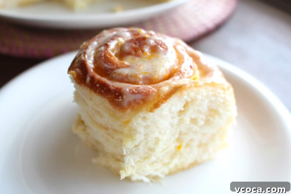 Zesty Lemon Rolls 2 45 degree angle shot of a fluffy lemon roll on a white plate, showcasing its golden-brown exterior and generous cream cheese frosting.