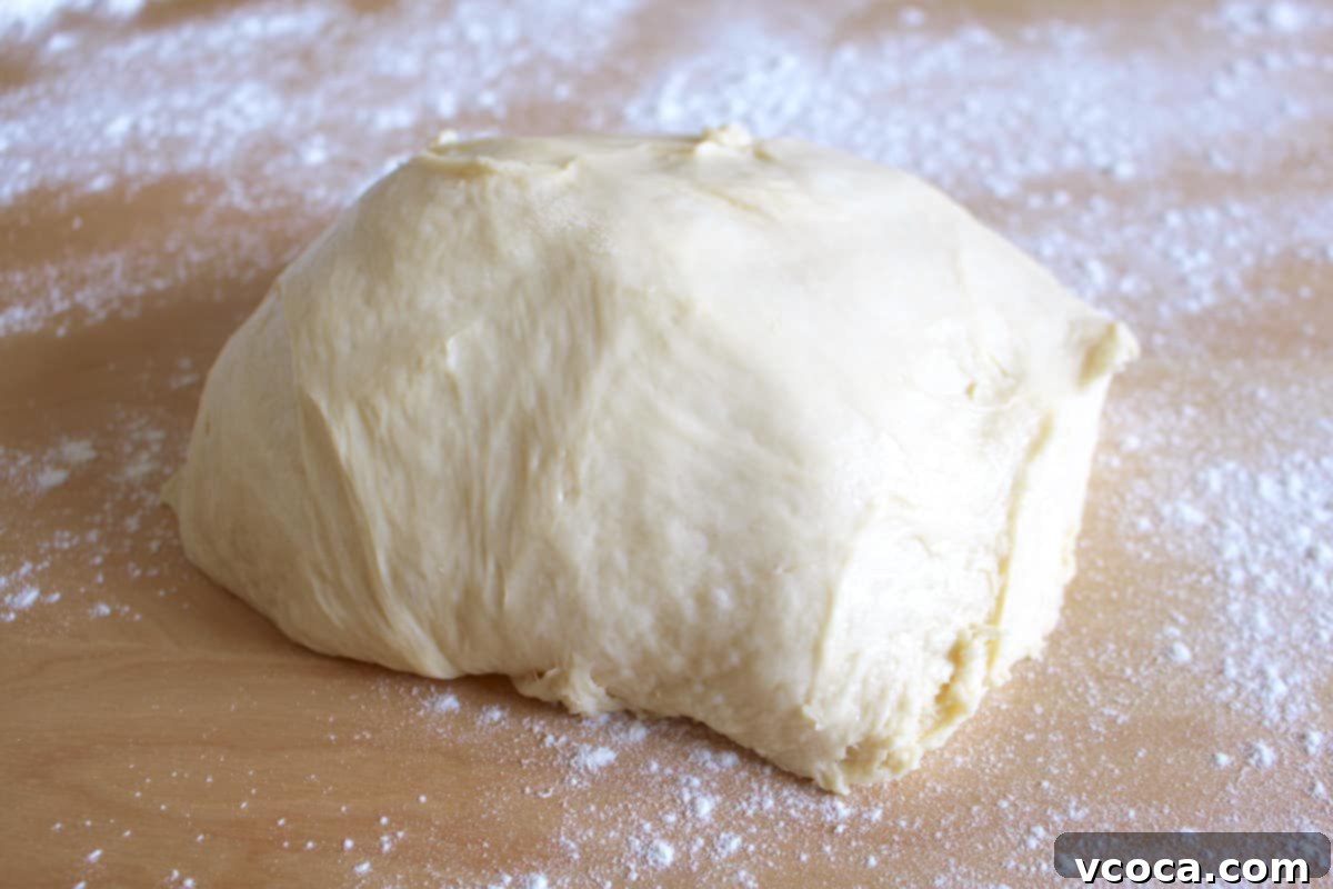 Zesty Lemon Rolls 3 A smooth, elastic ball of lemon roll dough resting on a lightly floured wooden surface, ready for the next step.