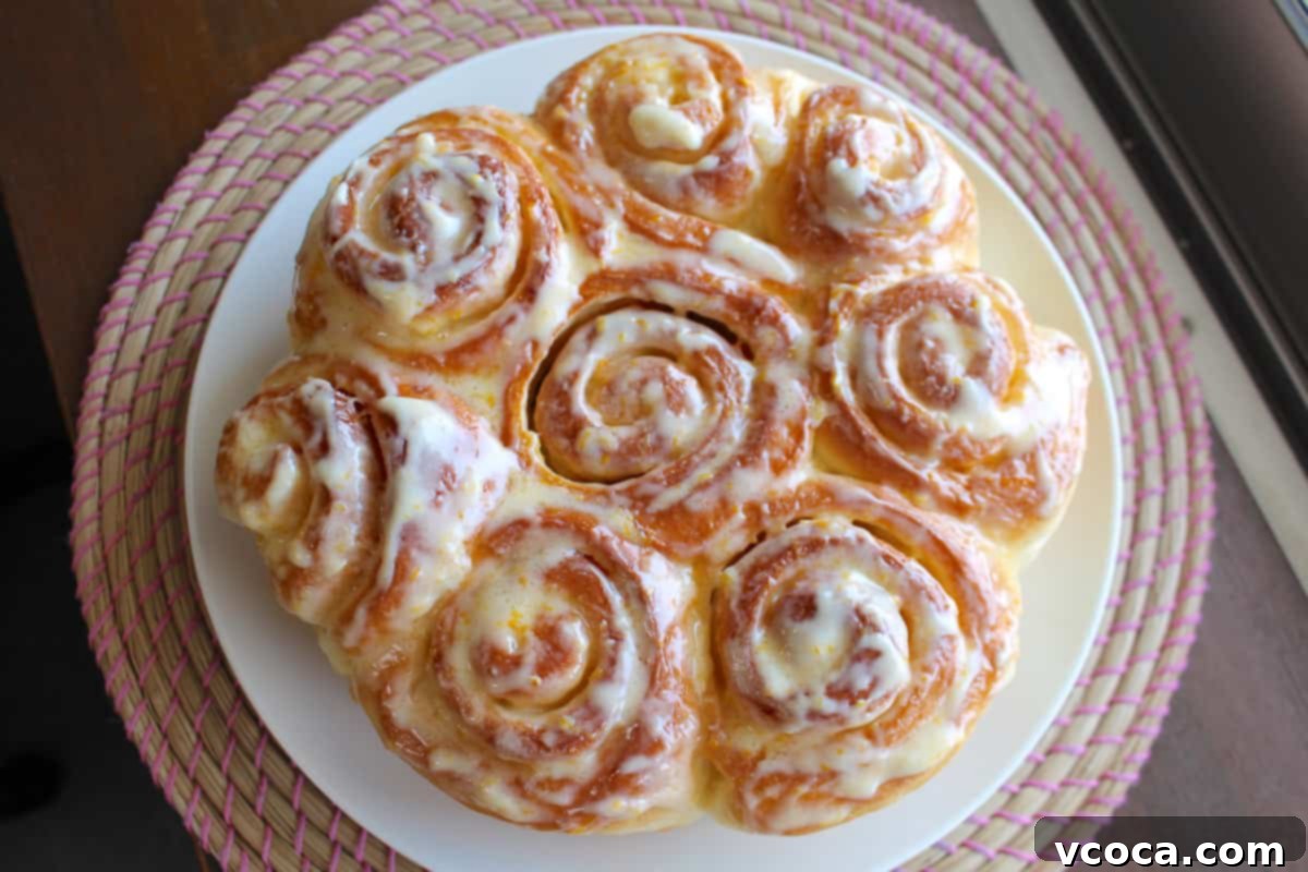 Zesty Lemon Rolls 7 Eight freshly baked lemon rolls artfully arranged on a pristine white plate, generously drizzled with luscious cream cheese frosting.