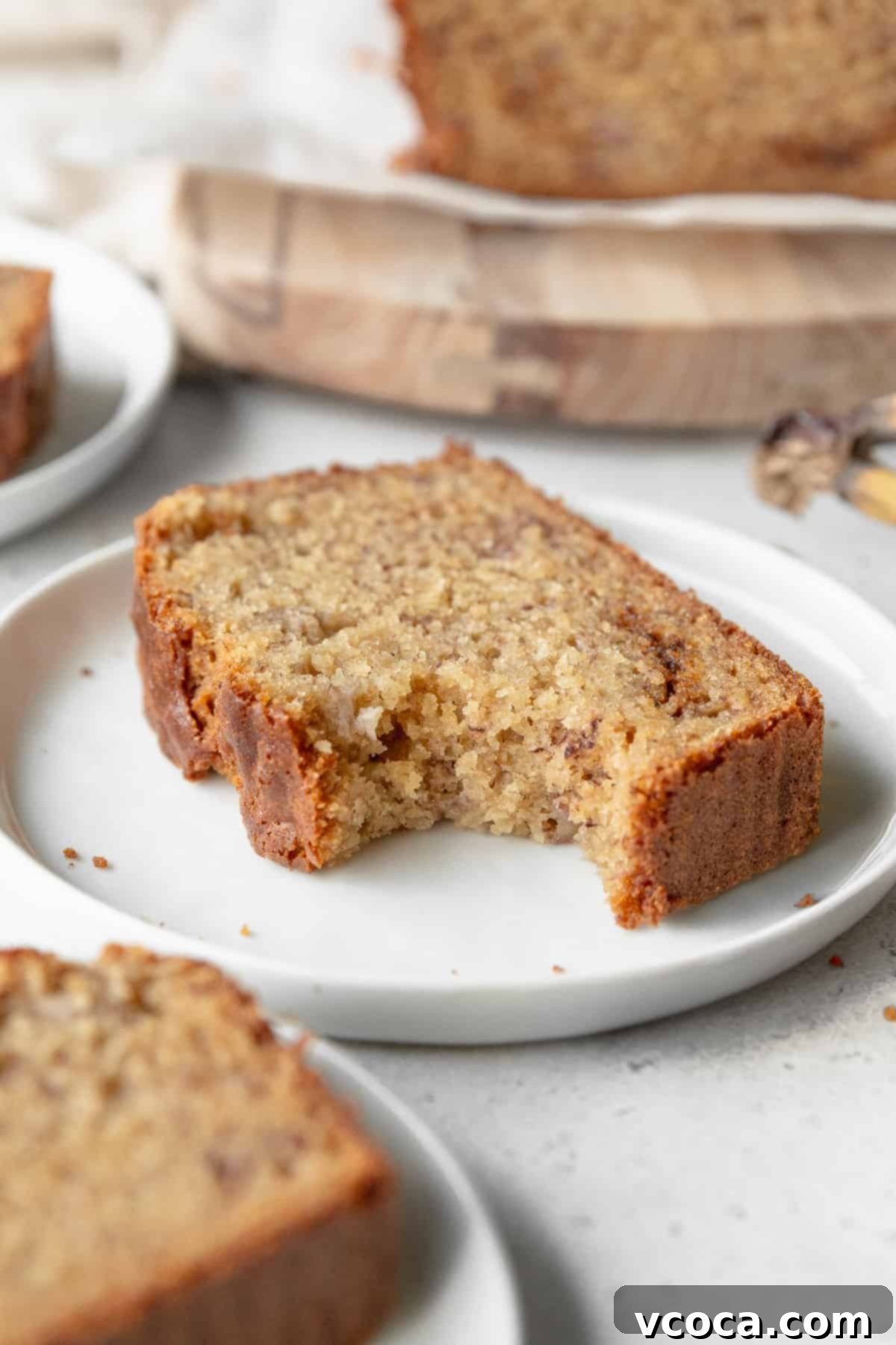 A bitten slice of gluten free banana bread on a small white plate.