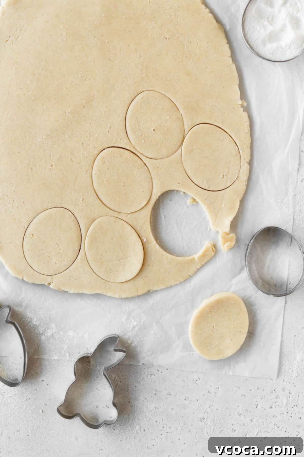 Joyful Easter Cookie Delights 7 Sugar cookie dough rolled out and shapes being cut with an egg-shaped cookie cutter.